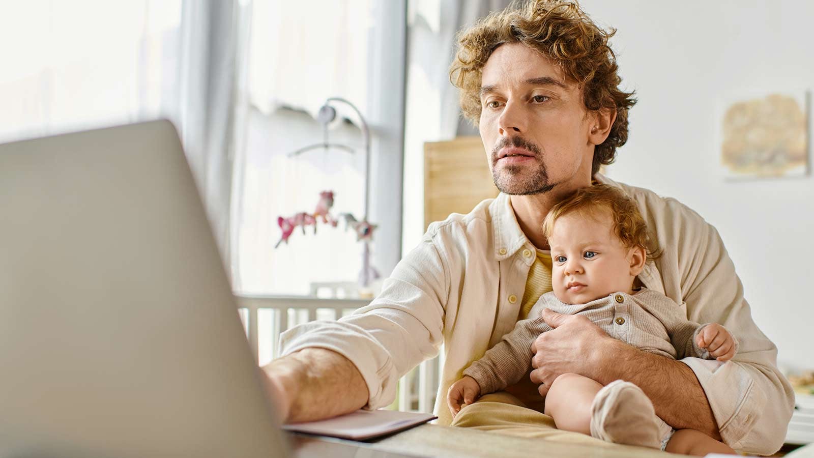Padre lavora al computer con figlio piccolo in braccio