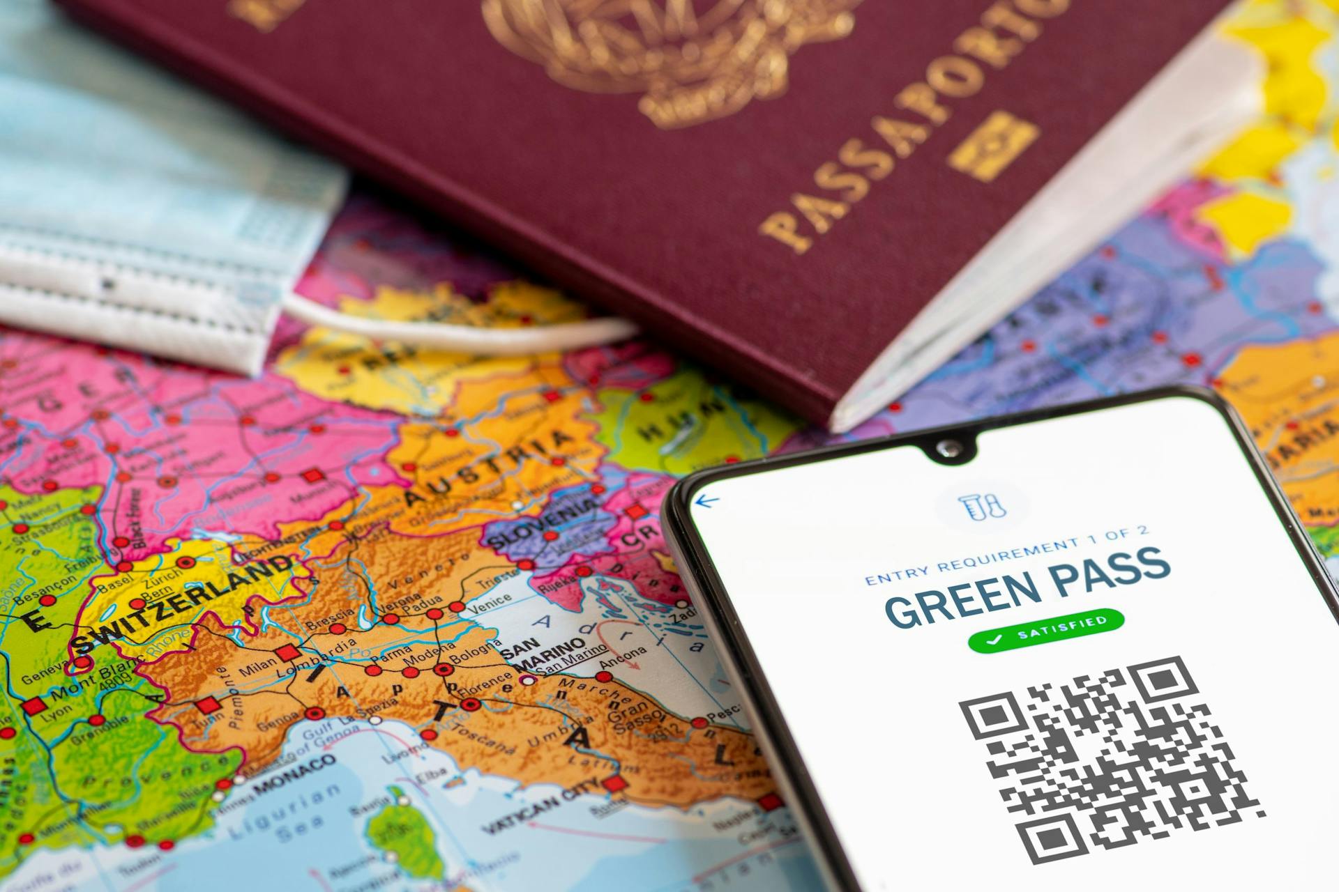 smartphone con immagine Green pass su cartina geografica, vicino a passaporto, mascherina
